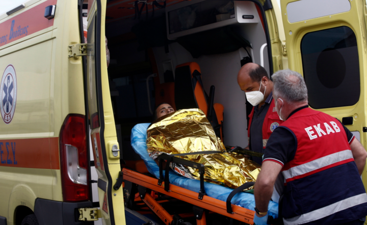 Sanitariusze z greckiego pogotowia ratunkowego przenoszą migranta do swojej karetki / autor: PAP/EPA/YANNIS KOLESIDIS